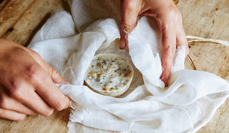 Photograph of hands and a bath melt made with oats, cocoa butter and dried flowers