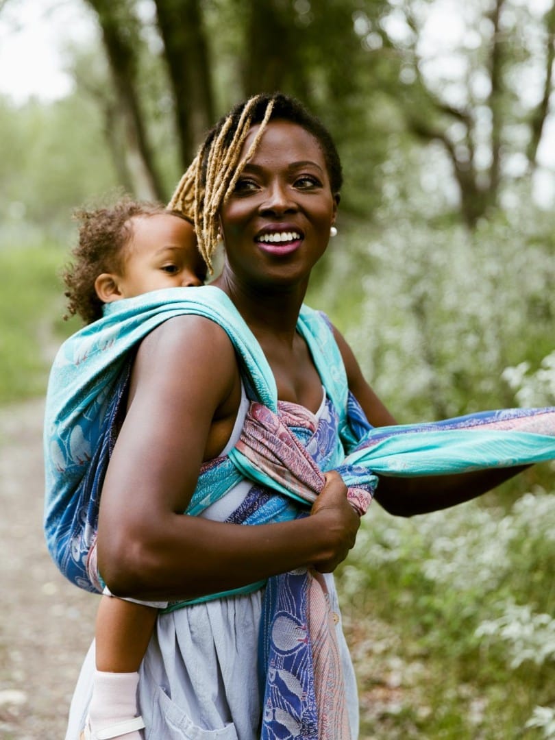 Photograph of a mother wearing a woven wrap with her baby on her back