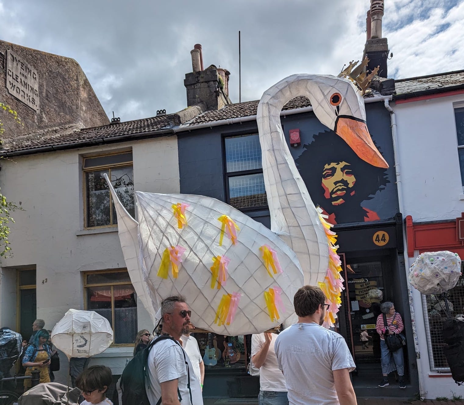 A photograph showing a large willow and tissue paper swan being walked through the streets of Brighton