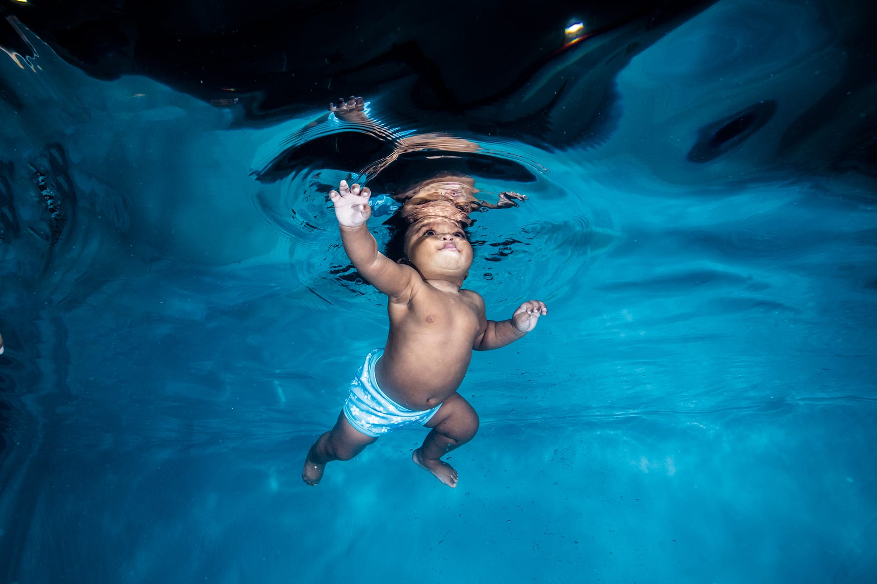 Photo shows a baby in a swimming pool, taken from underwater