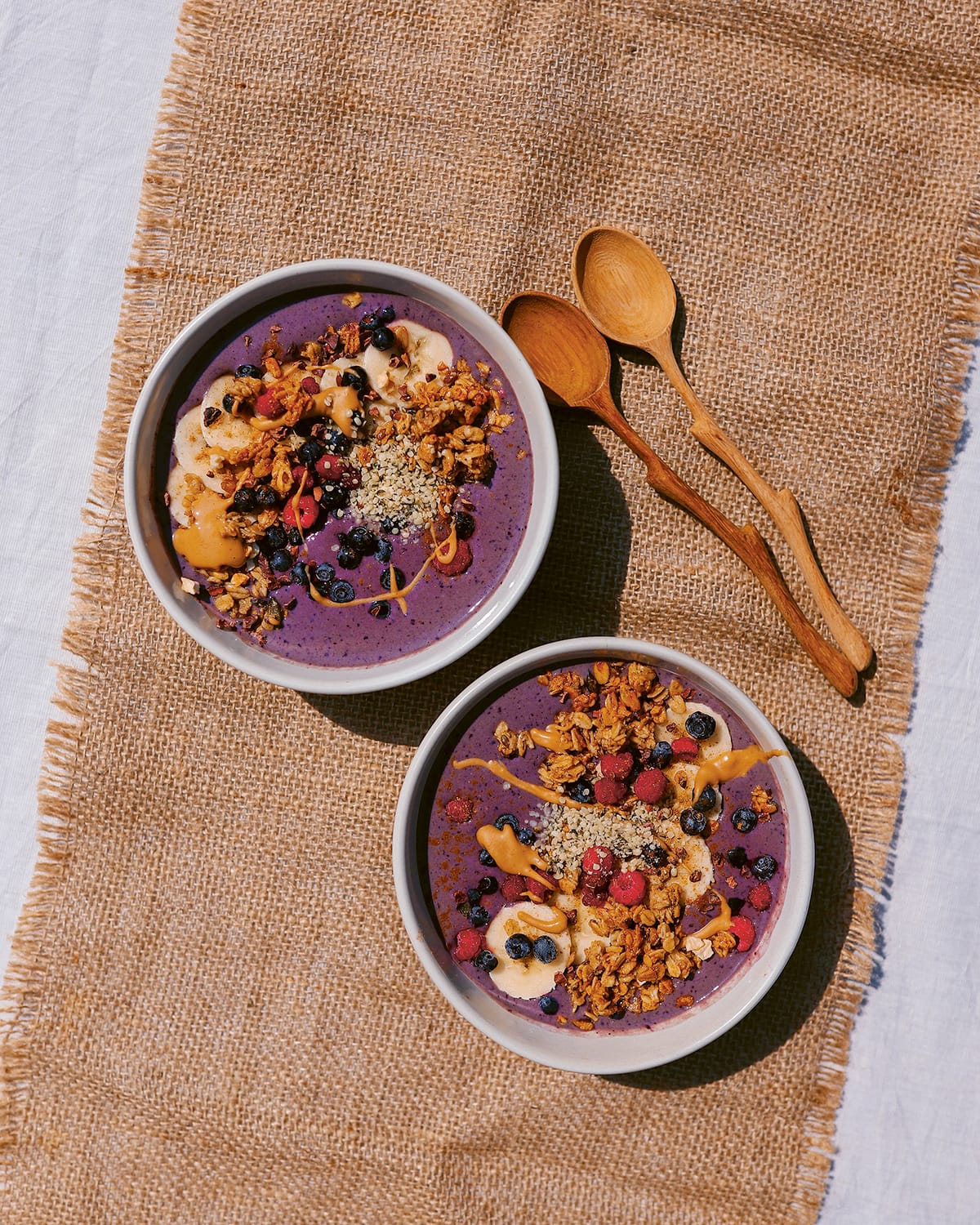 Photo shows a purple blueberry smoothie bowl with additional toppings on a hessian background