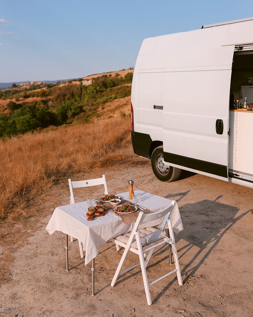 Photo shows a table laid for dinner with white tablecloth, outside a white camper van