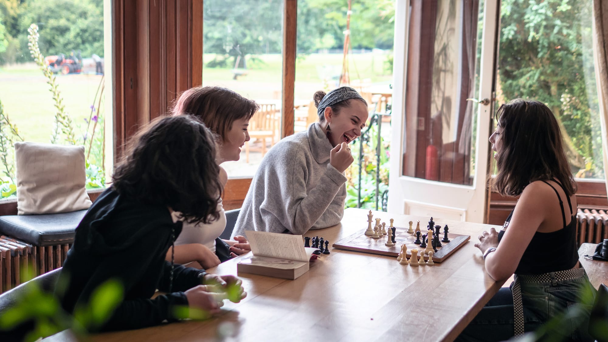 Group of students sitting round a wooden table playing chess and laughing