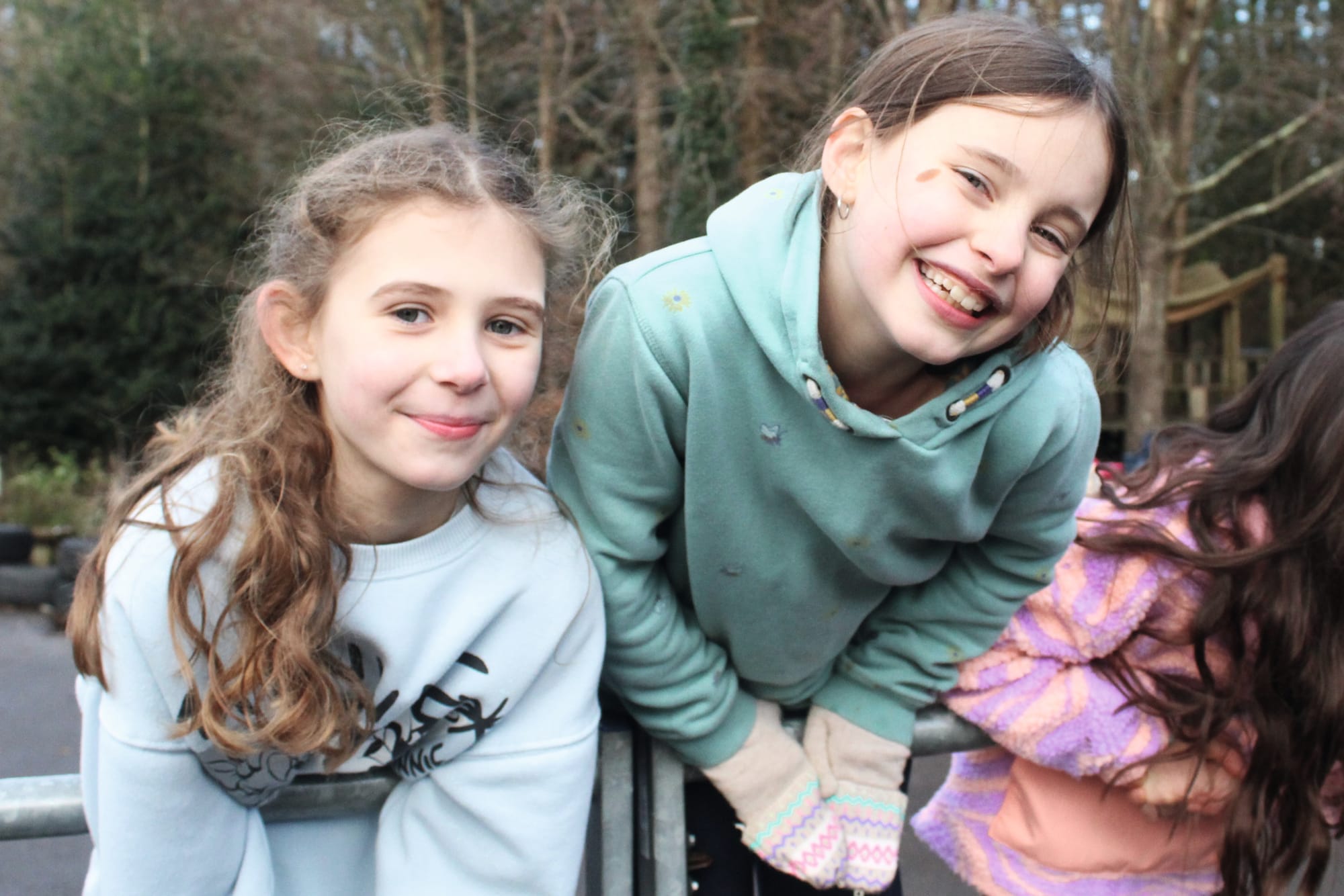 Photograph shows smiling children leaning on a gate in a school playground