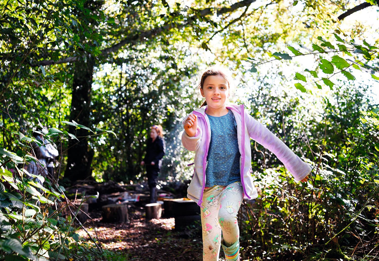 Photo of a child running through the woods with sunlight dappling the leaves