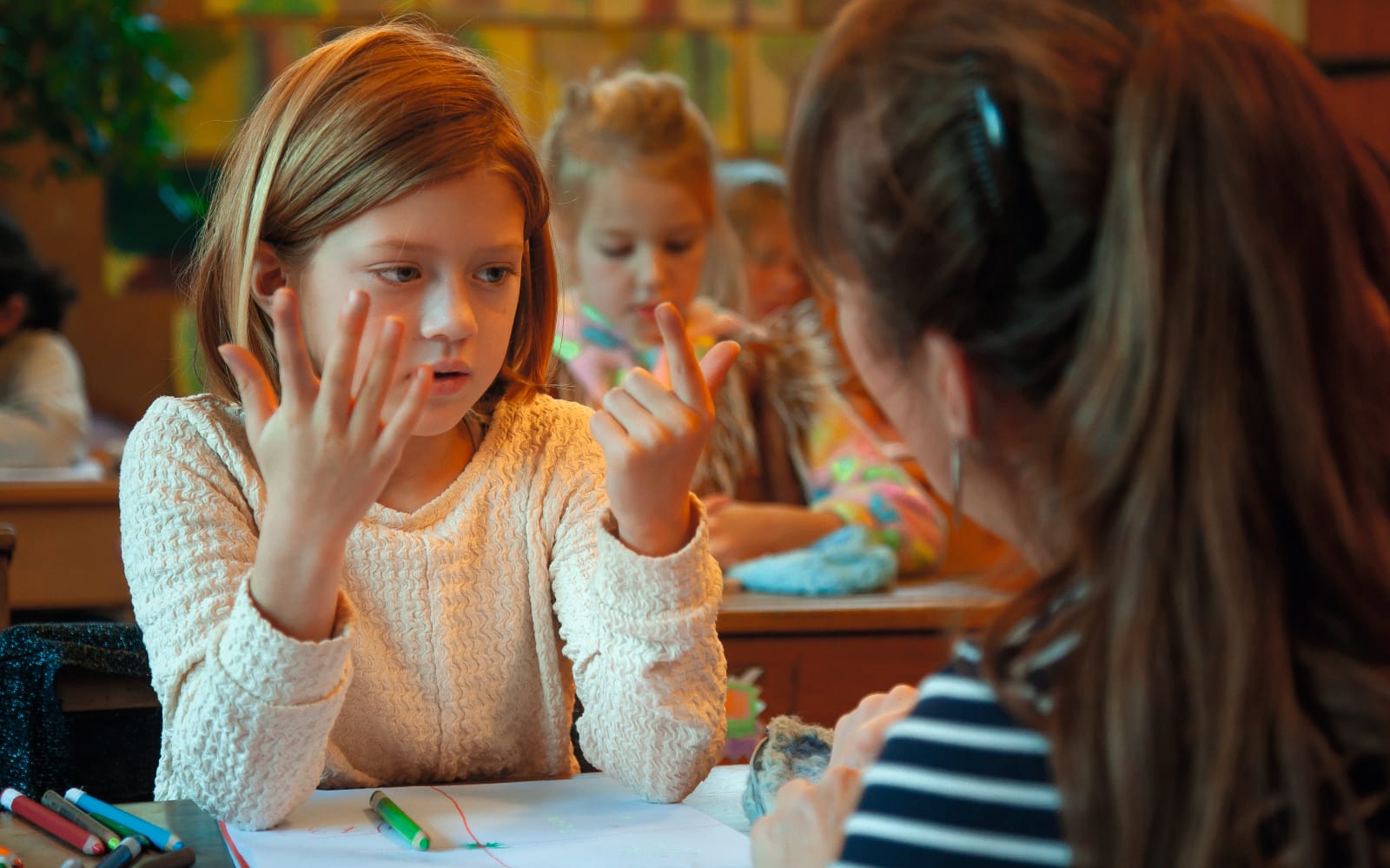 Photograph of a child in a classroom using her fingers to complete a mathematical problem