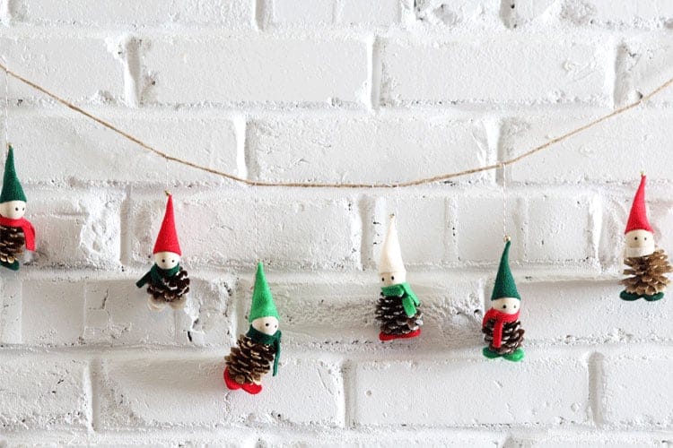 A series of elves made from pinecones and felt strung into a garland. They're wearing red and green hats.