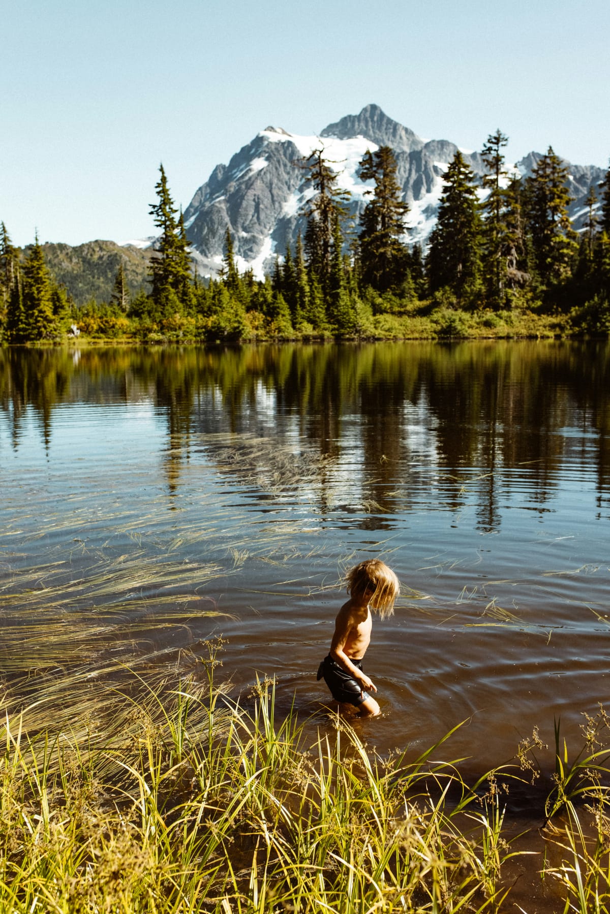 Magical mountain scene with a child wading in a lake in the foreground