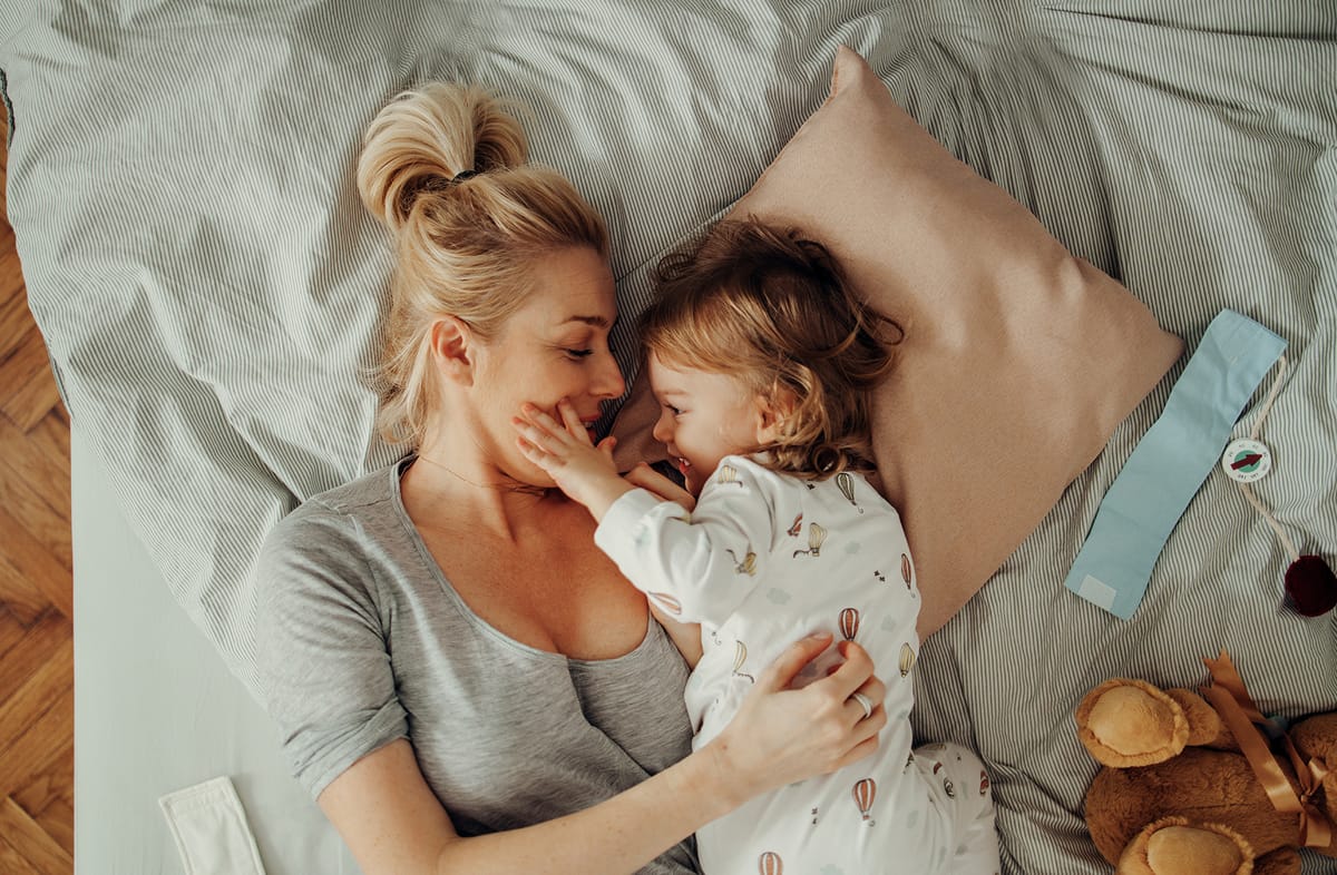 Photograph of a mother and child lying in bed, smiling at one another 