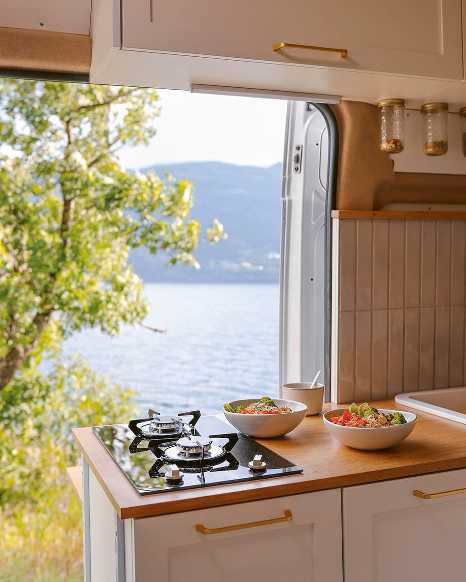 Photo shows a camper van kitchen with two ring hob looking out over a lake