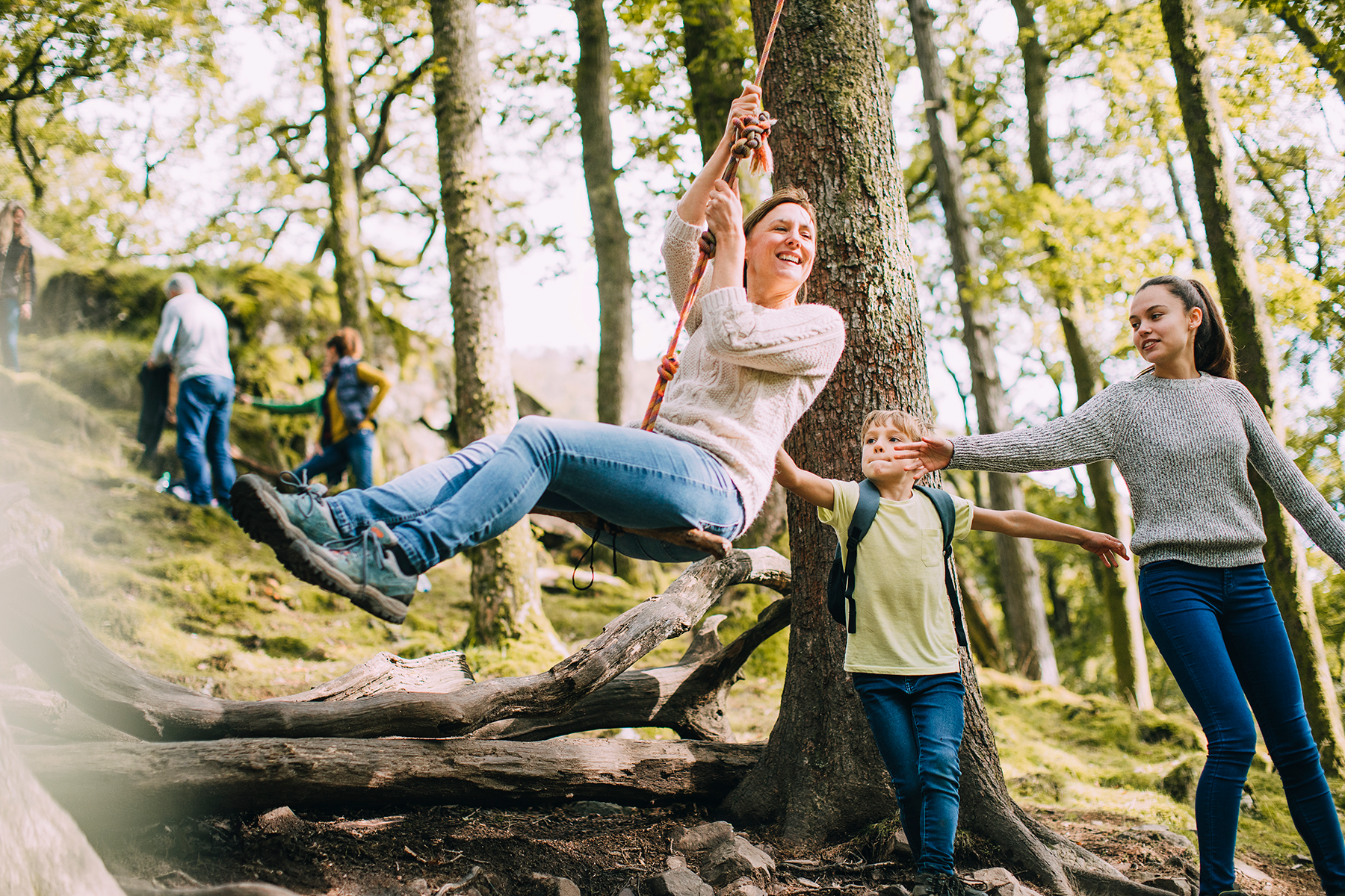 Photograph of a woman swinging on a rope swing suspended from a large tree, accompanied by her children