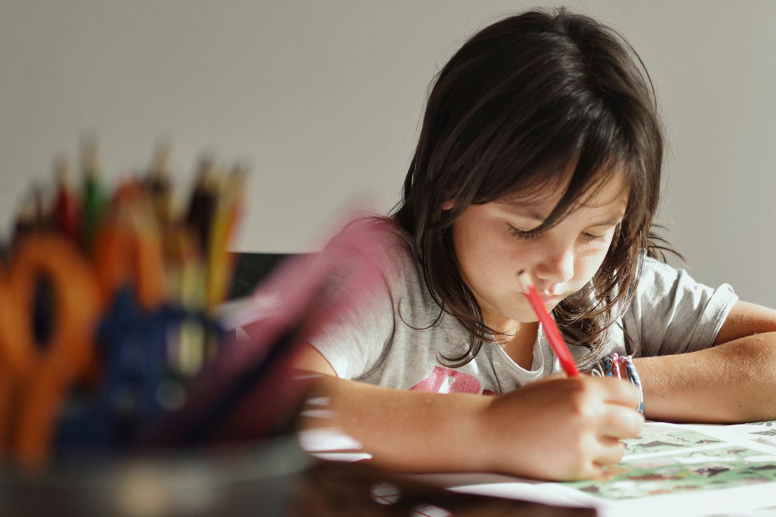 Photograph of a child with writing equipment in foreground, drawing on a worksheet with a pencil