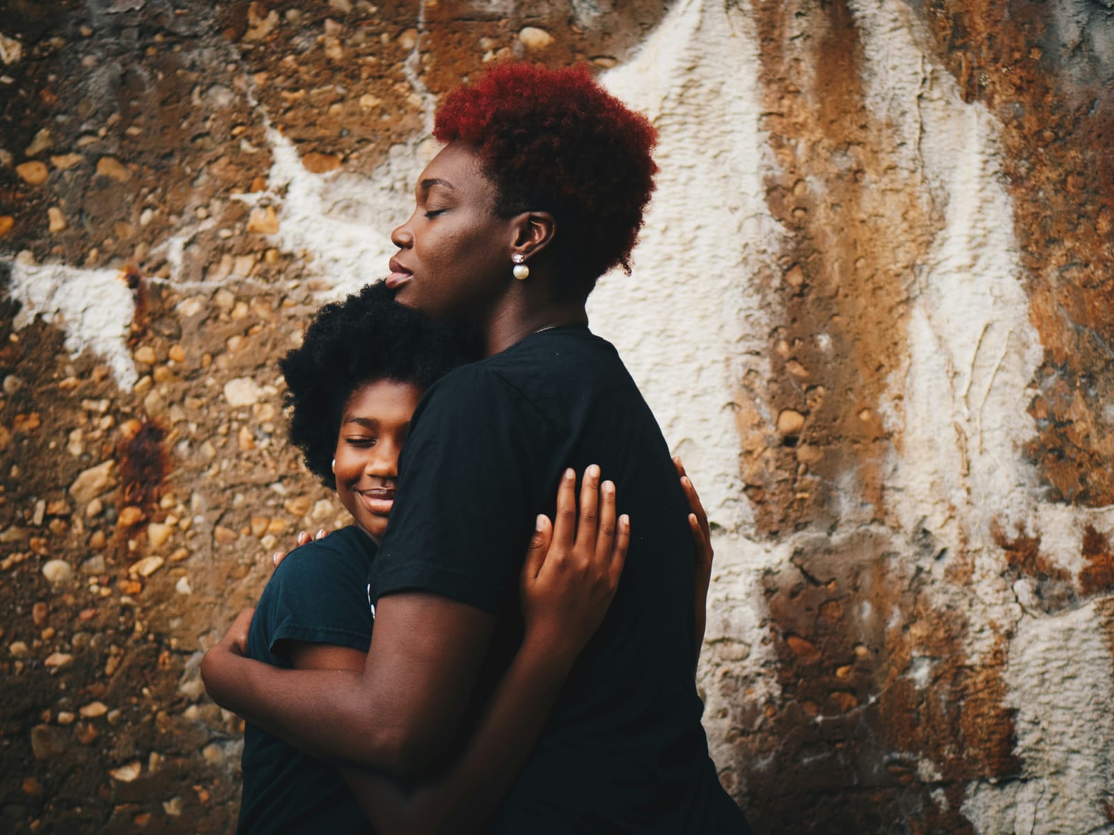 Mother and daughter embracing in front of a patchy concrete wall