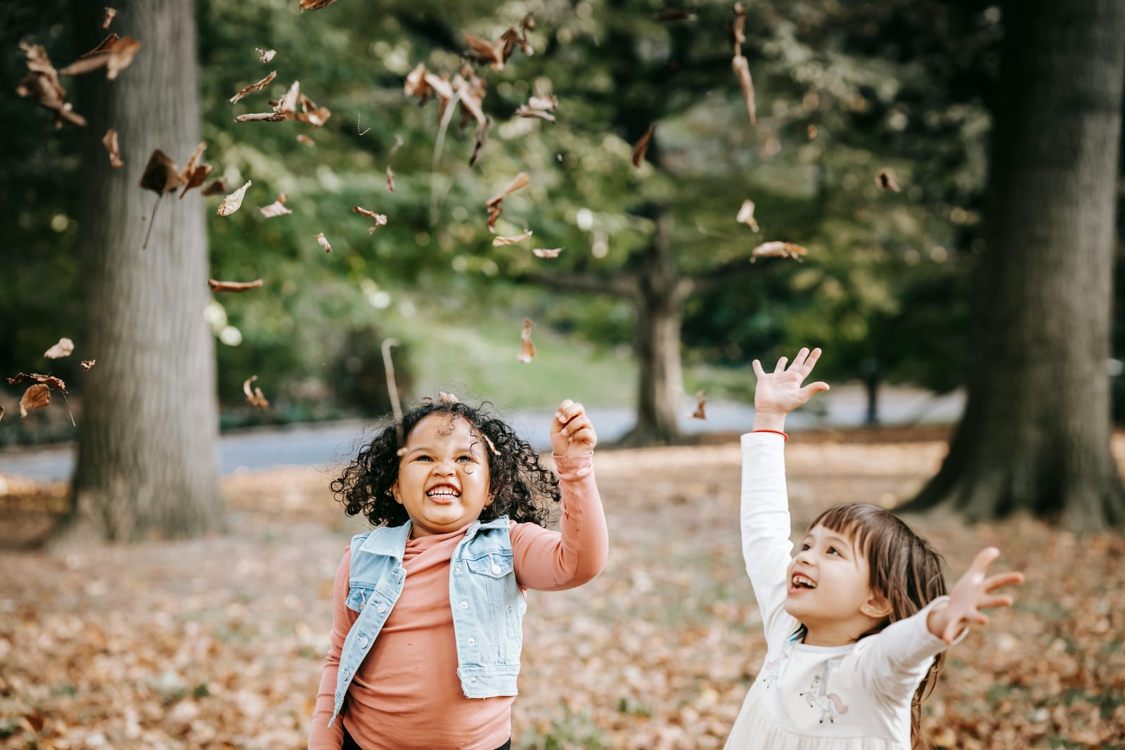 Photograph shows two children playing with autumn leaves and looking happy