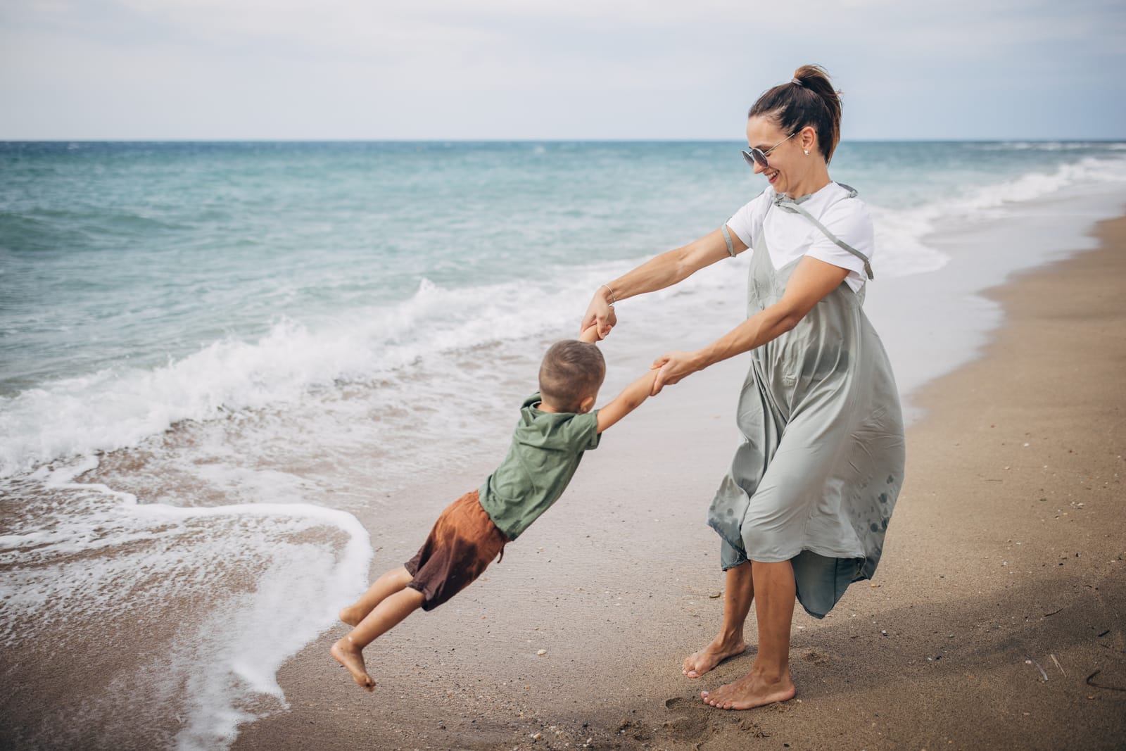 Photograph of a mother standing by the shoreline happily swinging her child around