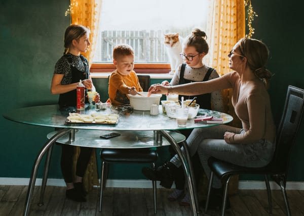 Photograph of an unschooling family sitting around a table baking together, overlooked by the family cat