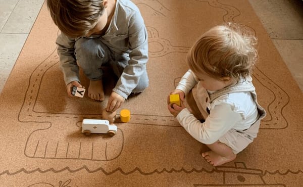 Photograph of two children playing with wooden vehicles on a cork play mat