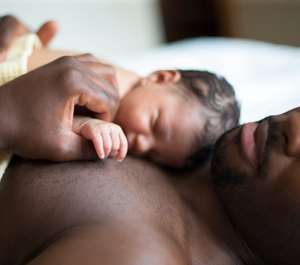 A baby lies on their father's chest receiving skin-to-skin contact