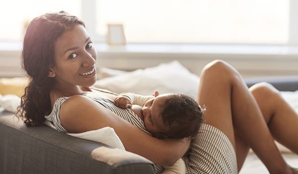 Mother on a sofa sits and breastfeeds her baby