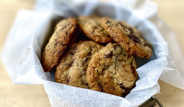 Photograph of a tiffin tin packed with baking parchment and chocolate chip cookies