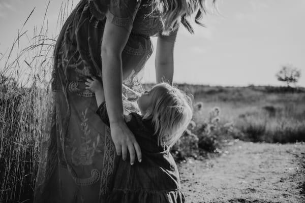 Photograph of a pregnant woman bending down to pick up her young toddler