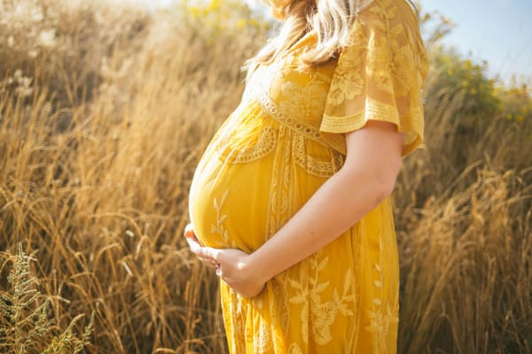 Pregnant women in a yellow dress stands in a meadow of grasses