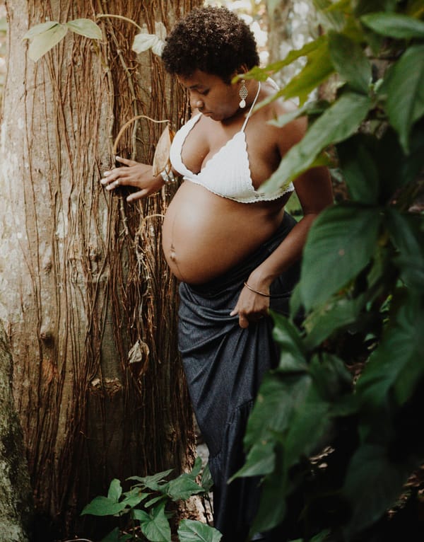 Portrait of a pregnant woman amidst foliage with a tall tree trunk beside her