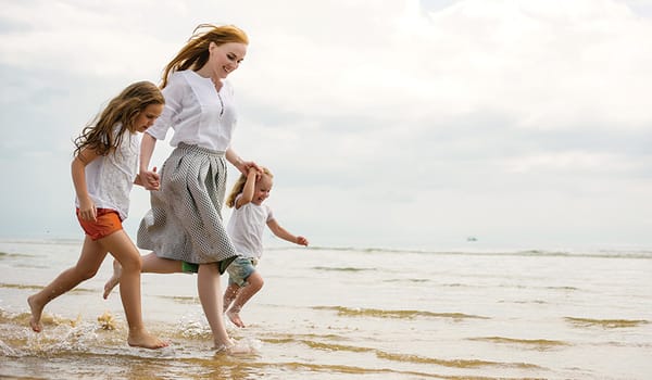 A mother runs along the beach with her two daughters looking joyful
