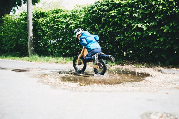 A young child rides a balance bike through a muddy puddle