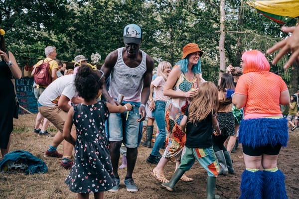 Photograph of children dancing in a woodland, at a festival, amidst the trees