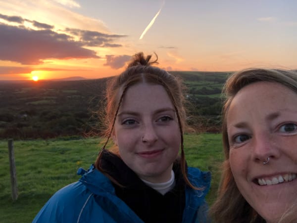 Photograph of a mother and her daughter on Mynydd Carningli at sunrise, with sun glowing orange in background