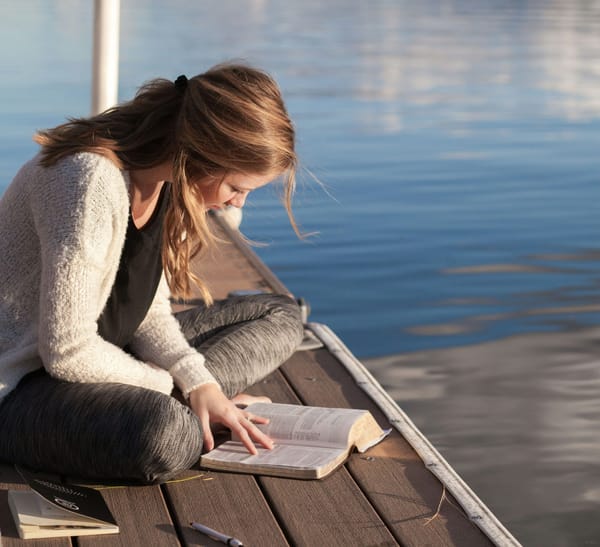 Photograph of a woman on a jetty reading a book