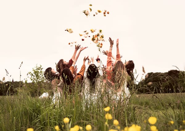 Photograph of a women's circle standing together in a field and throwing petals into the air