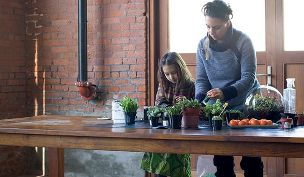 Photograph of a mother and her daughter standing at a table making a terrarium, surrounded by plants