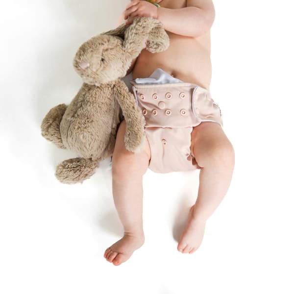 Photograph of a baby's torso and legs showing a washable cloth nappy and teddy bear