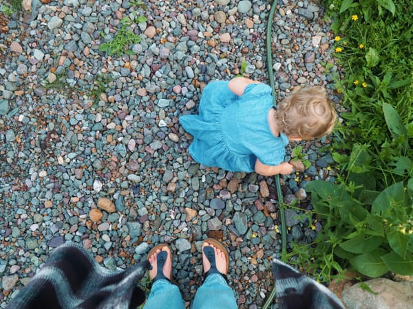 Photograph of a mother's feet looking down at her toddler exploring the ground