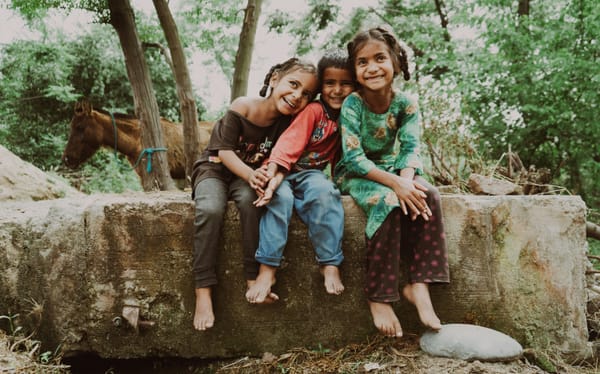 Photograph of 3 children sitting on a rock grinning, with a horse tied up to a tree behind them