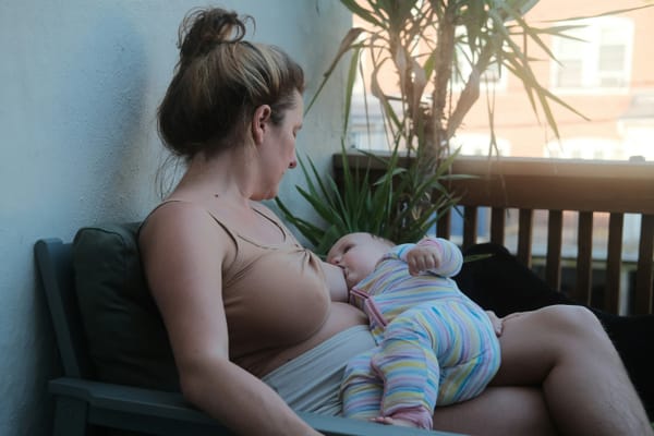 Photograph of a woman sitting on a chair on a balcony breastfeeding her young child