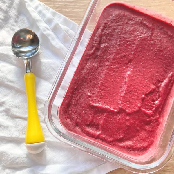 Photograph shows a dish full of blackberry ice cream with a yellow ice cream scoop nearby, against a white tablecloth