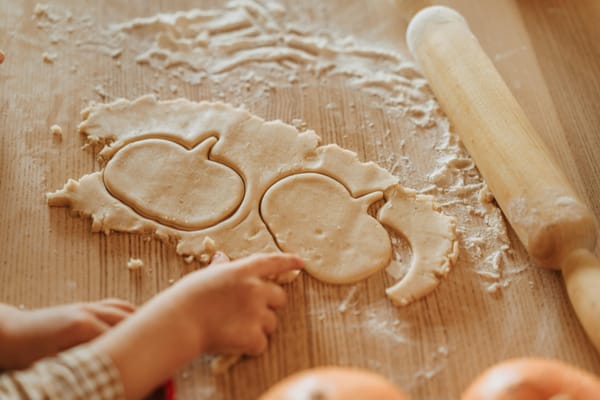 Photo of a child's hands cut out some dough, on a floured wooden surface with rolling pin nearby